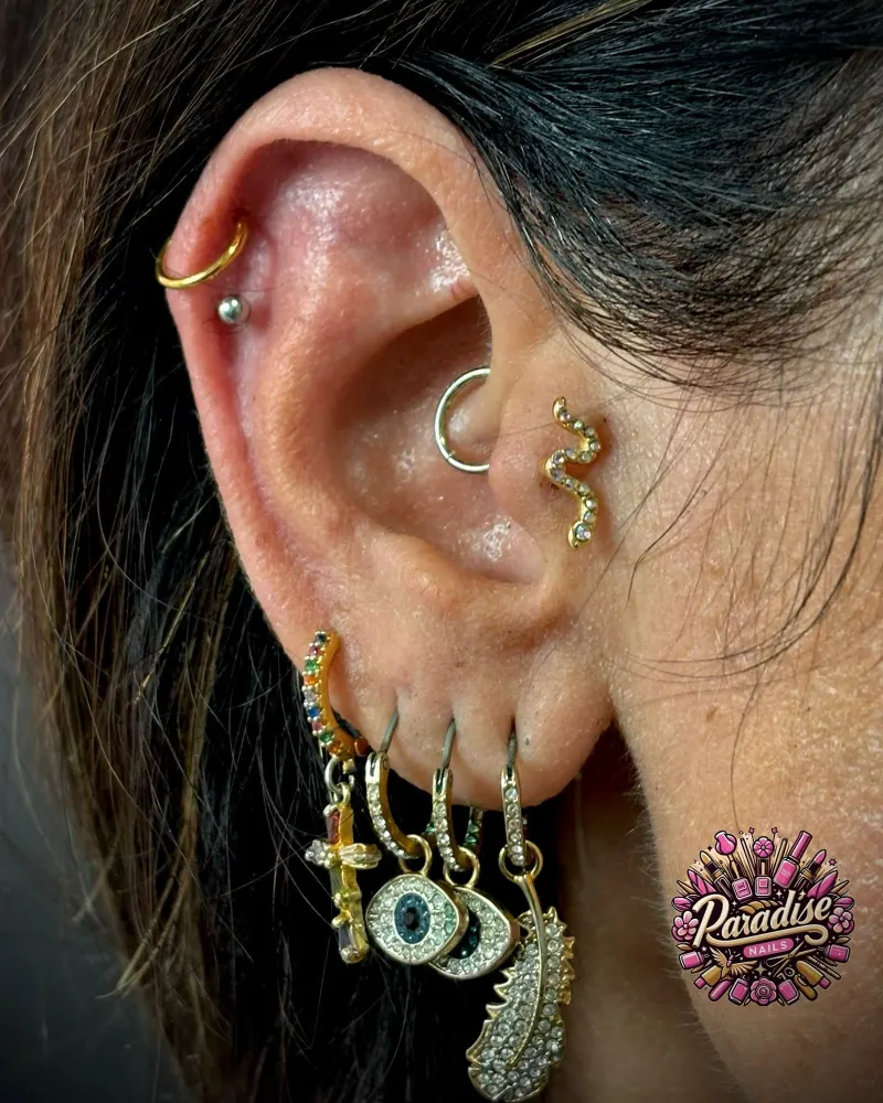 Composición de piercings en la oreja con aros y joyas doradas
