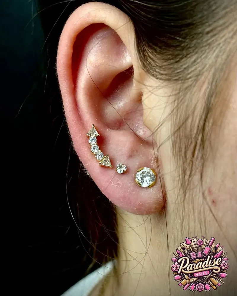 Composición de piercings en el lóbulo y el hélix con joyas doradas