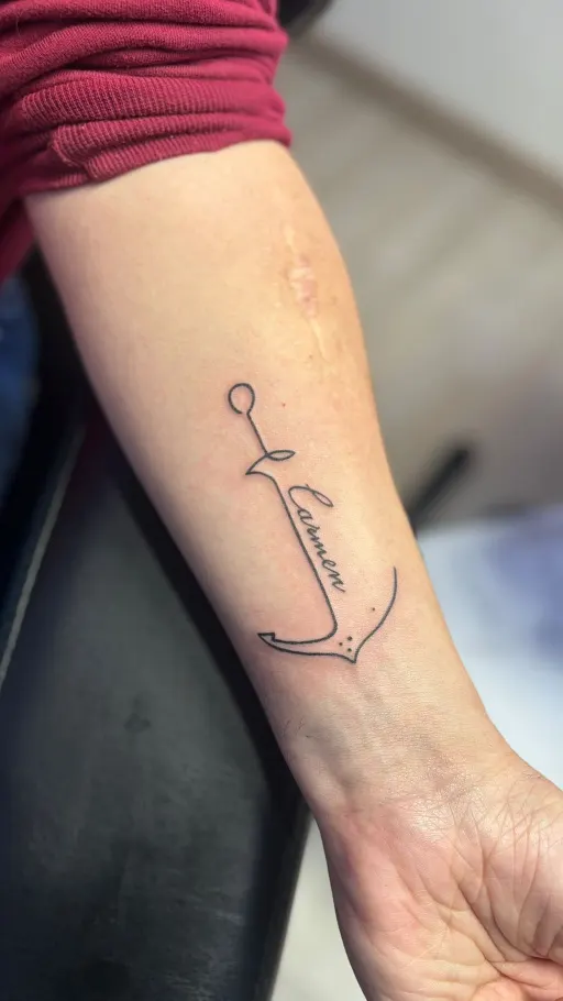 Tatuaje minimalista de un ancla con lettering en el antebrazo