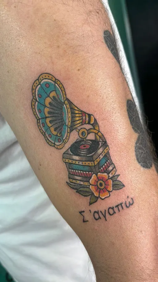 Tatuaje neotradicional a color de un gramófono con flores y lettering en el antebrazo