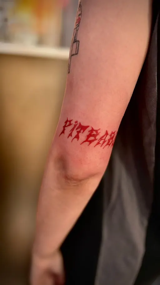 Tatuaje de lettering en tinta roja en el brazo