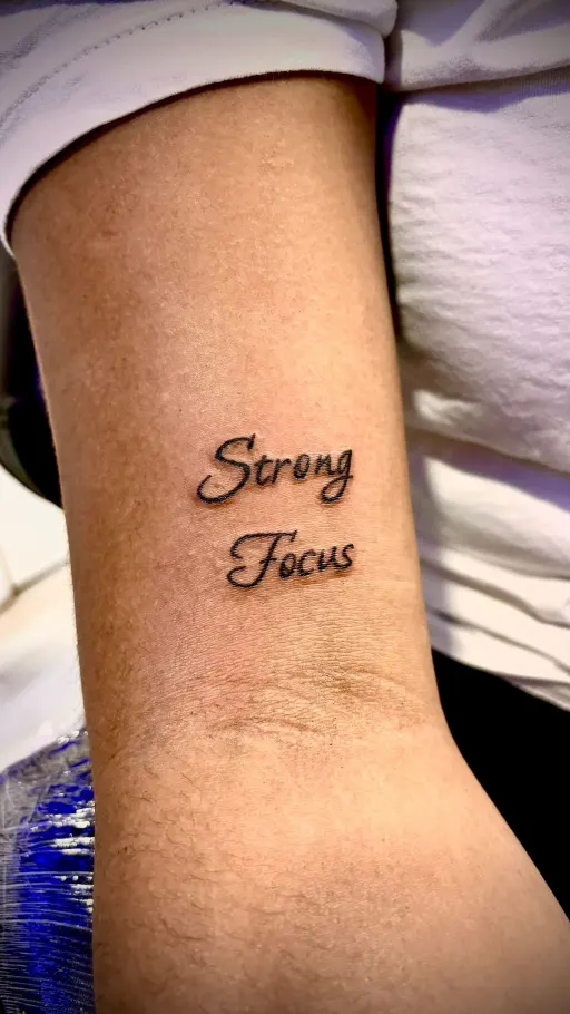 Tatuaje de lettering con la frase Strong Focus en el brazo