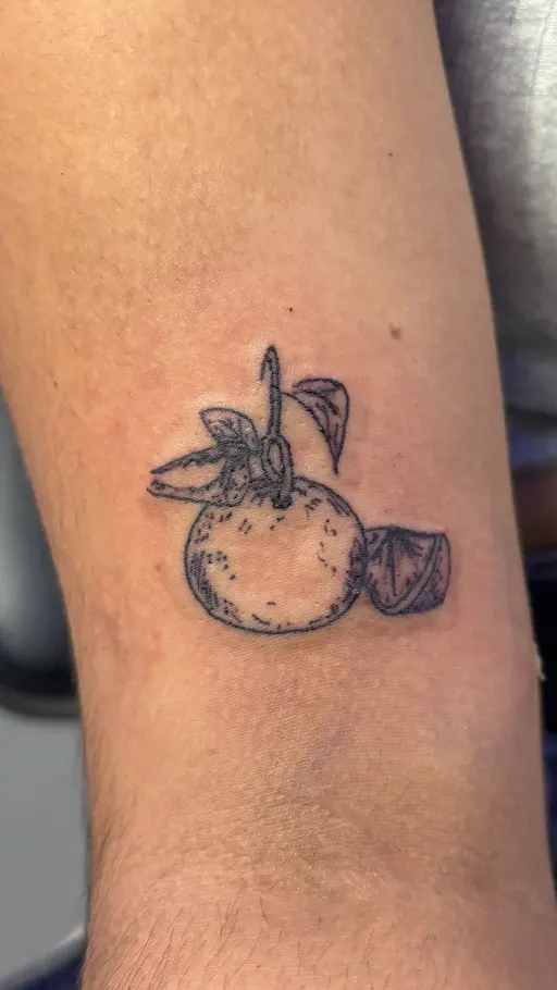 Tatuaje fine line de una naranja con hojas en el brazo